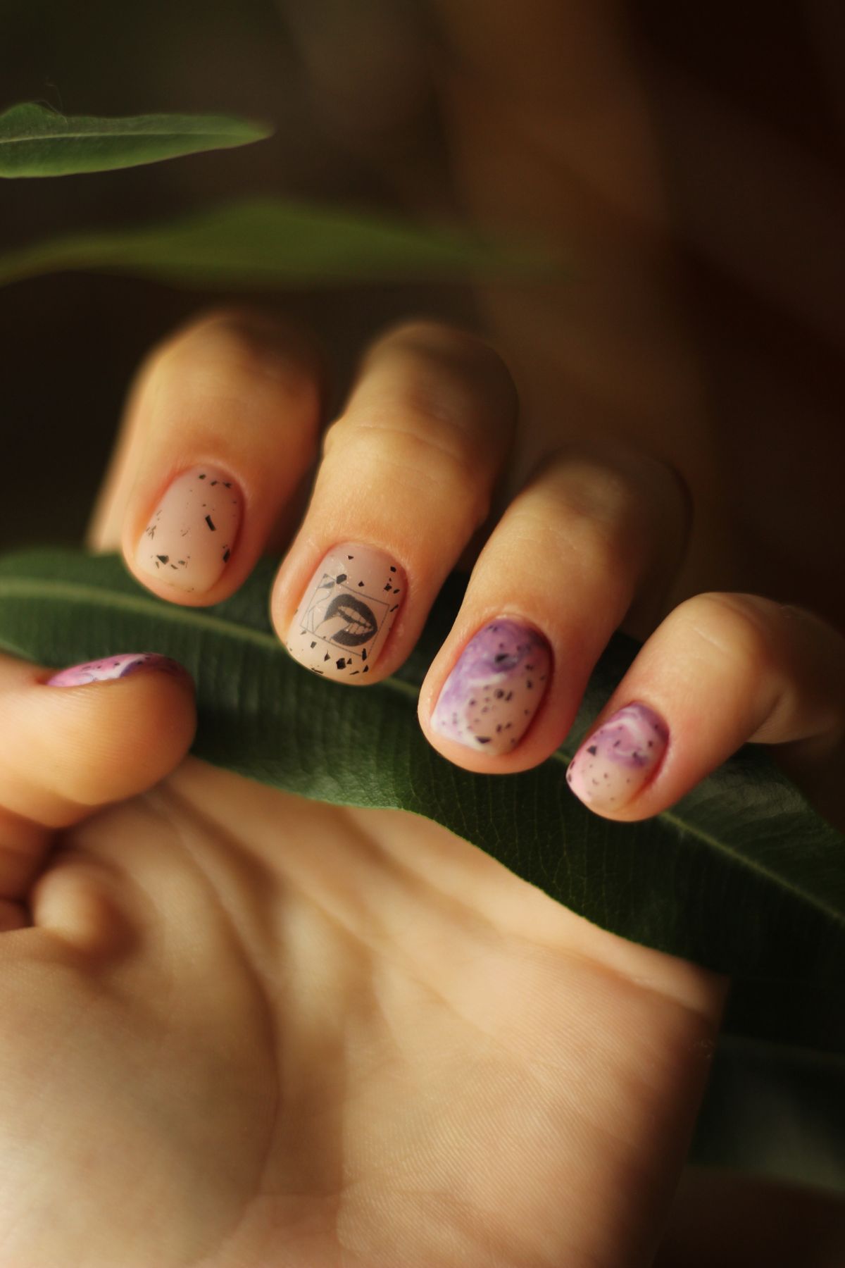 Close-up of a hand with artistic manicure featuring floral patterns, holding a green leaf.