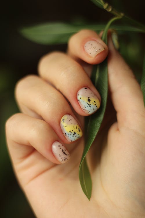 A Hand with Colorful Nail Art Holding Green Leaf