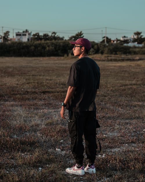 Free A young man wearing casual clothing stands on a grassy field during the day. Stock Photo