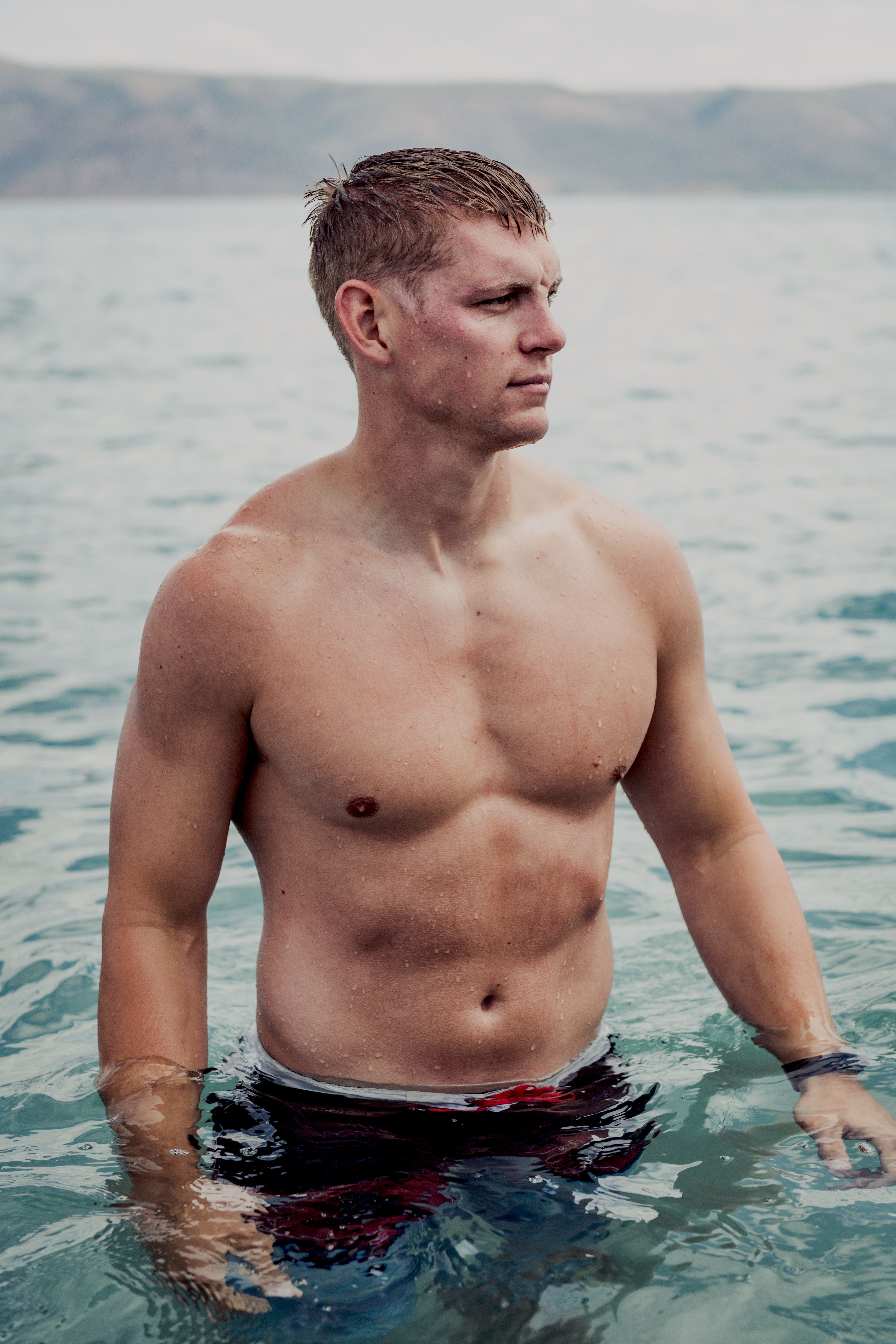 Shirtless man enjoying the ocean views, displaying athletic physique and tranquility.