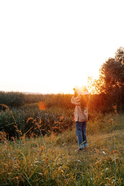 Woman in Brown Sun Hat and Blue Denim Jeans Standing on Green Grass Field