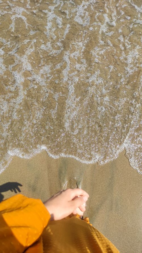 Free A hand touches the sand as gentle ocean waves approach, a serene beach scene. Stock Photo