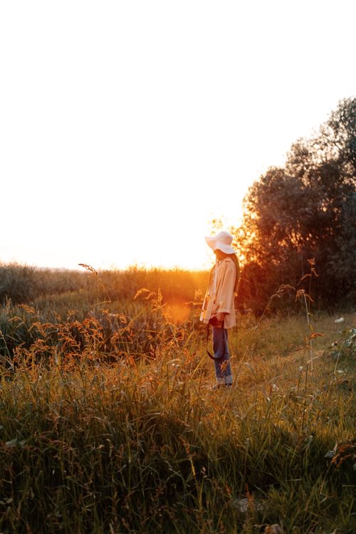 Free A woman stands in a grassy field at sunset, capturing the calm beauty of autumn. Stock Photo