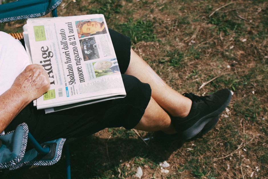 Senior holding a newspaper while sitting outdoors in Folgaria, Italy.