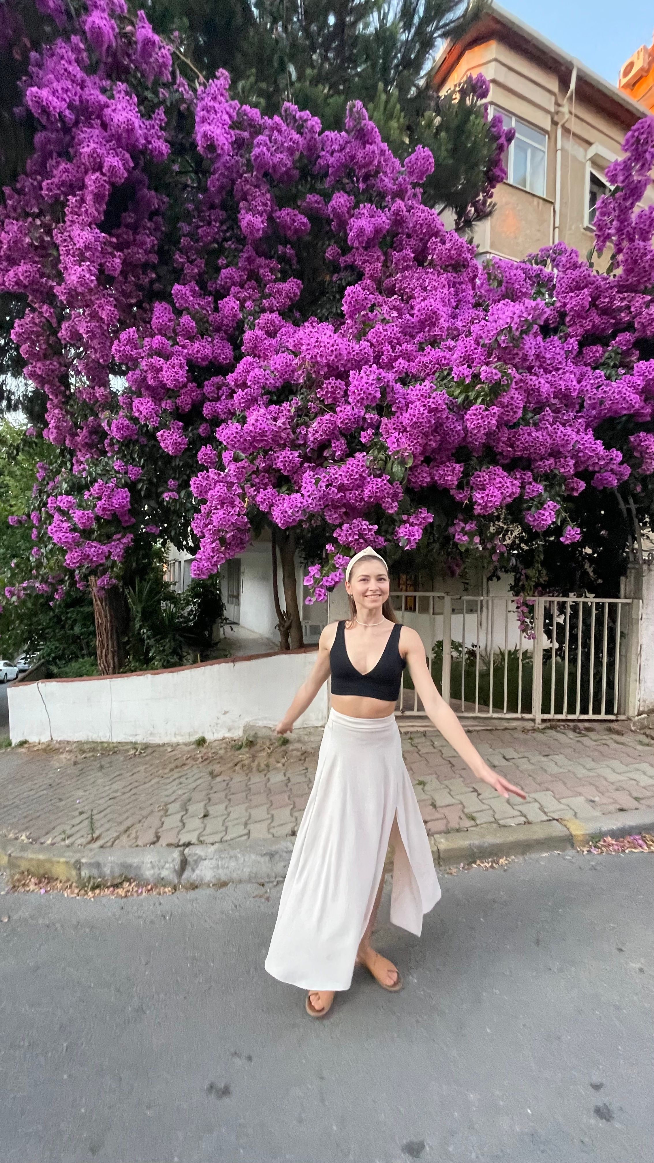 A young woman smiles joyfully under a vibrant purple bougainvillea, capturing the essence of Istanbul streets.