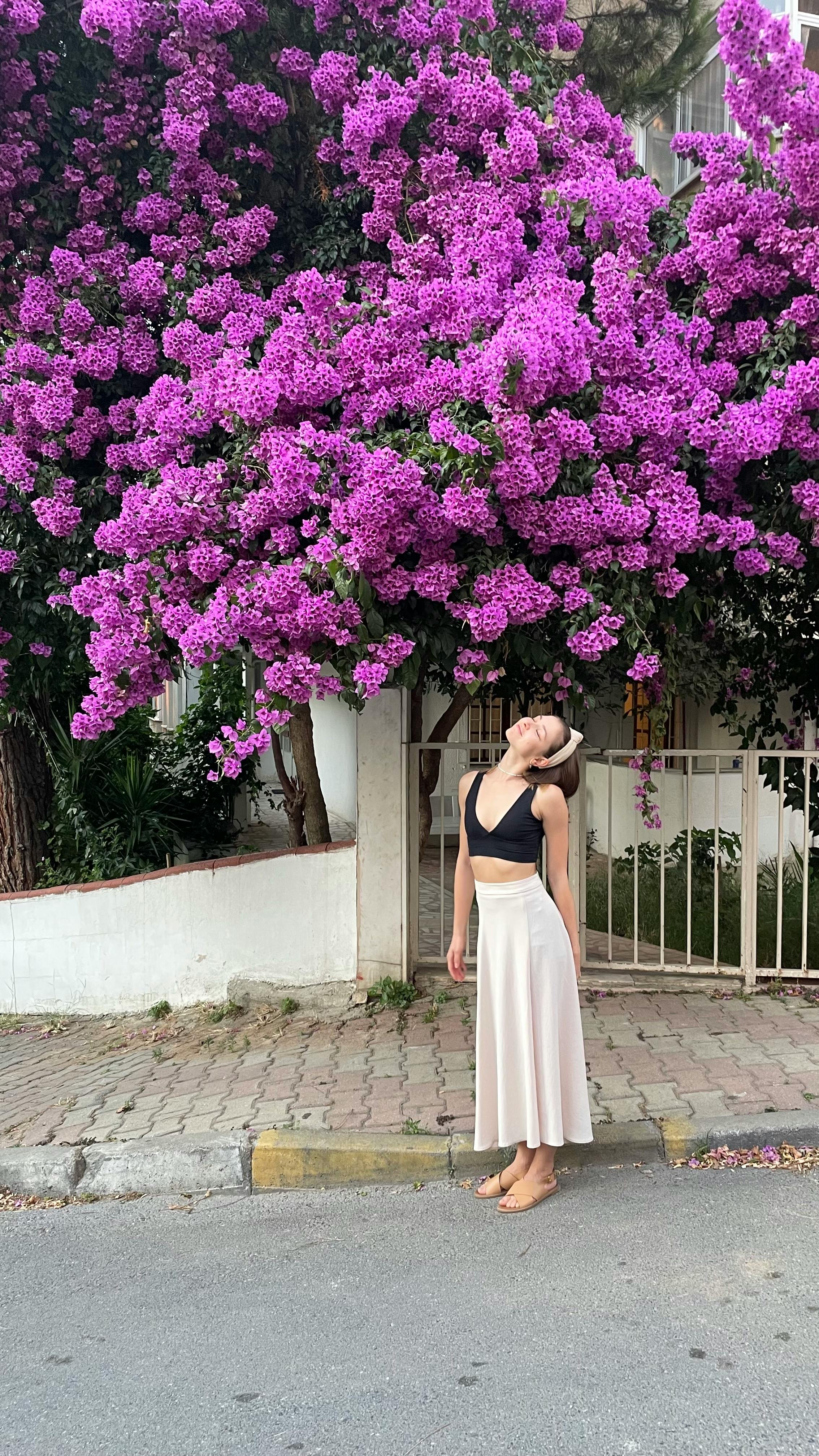 A woman gazes up at beautiful purple blossoms in a serene street setting in Ankara, Turkey.