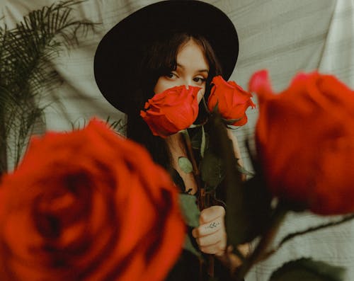 Close Up Photo of Woman Wearing Black Hat Holding Roses
