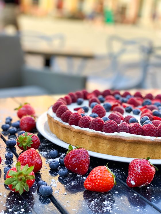 Tart topped with raspberries and blueberries over cream, with strawberries scattered on the table