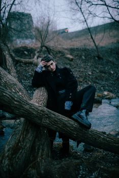Model in stylish winter attire sits contemplatively on a tree, capturing a moody fashion vibe.