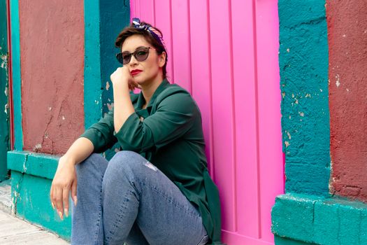 Woman in Green Hoodie and Gray Pants Sitting on Red Wooden Wall