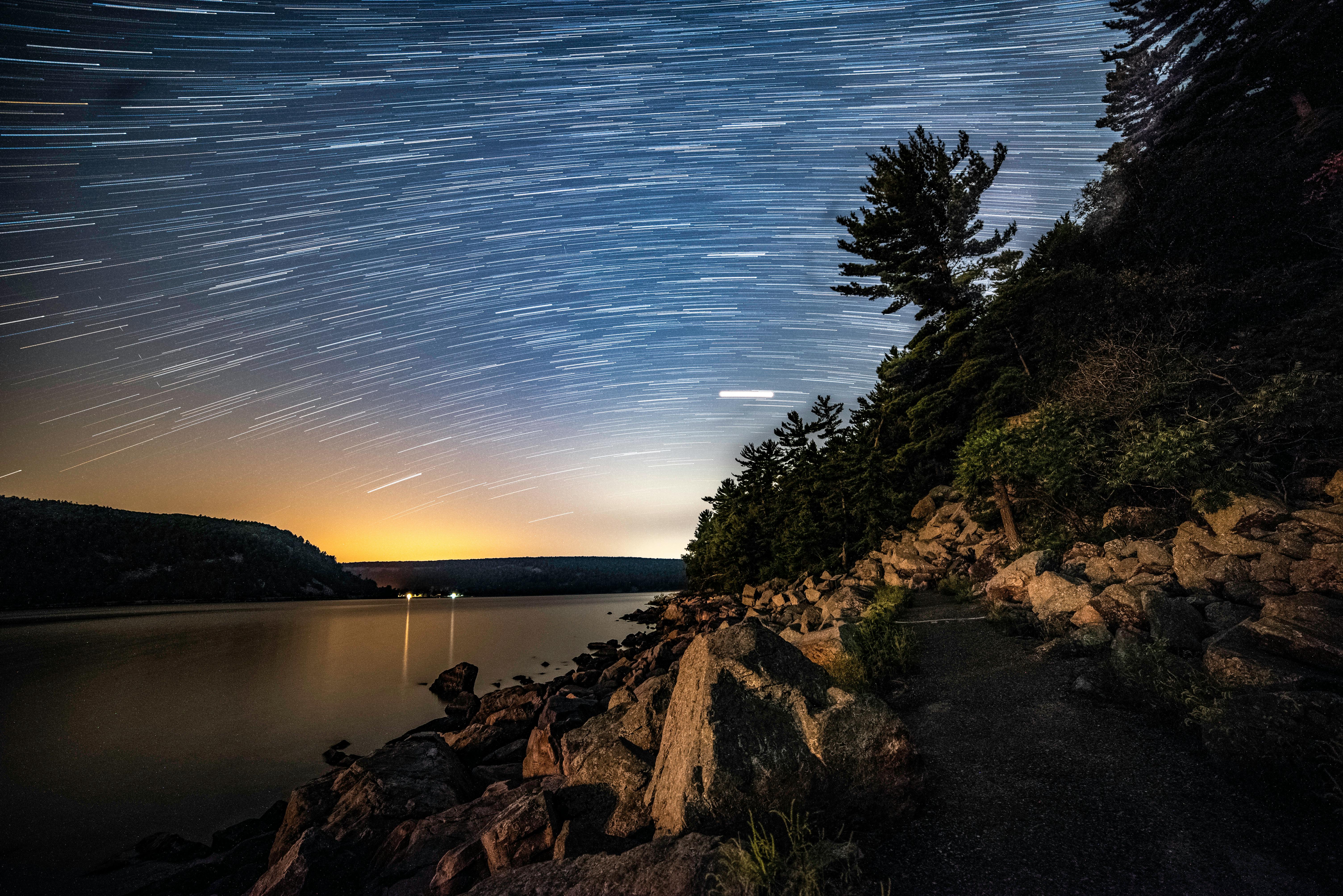 Captivating star trails over a tranquil lake with reflections, rocky shores, and silhouettes in Wisconsin.
