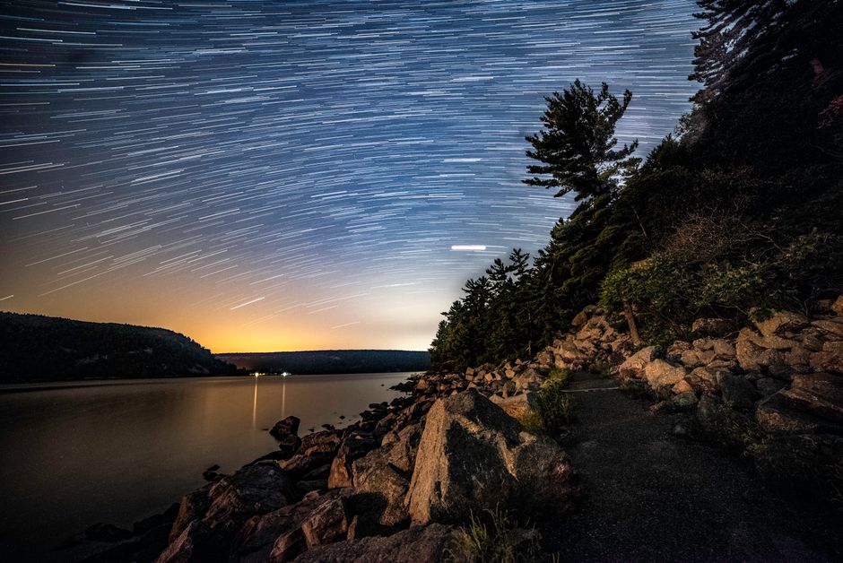 Captivating star trails over a tranquil lake with reflections, rocky shores, and silhouettes in Wisconsin.