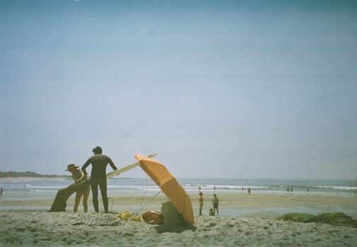 Relaxing beach scene with surfers, umbrellas, and ocean waves on a sunny day.