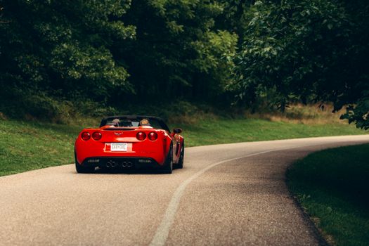 A red sports car drives on a tree-lined winding road during daylight, exuding adventure.
