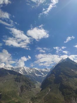 Stunning aerial view of snow-capped mountains and blue sky with fluffy clouds, perfect for adventure themes.