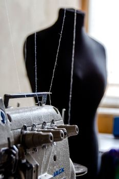 Close-up of a sewing machine with a mannequin in the background in a tailor's workshop.