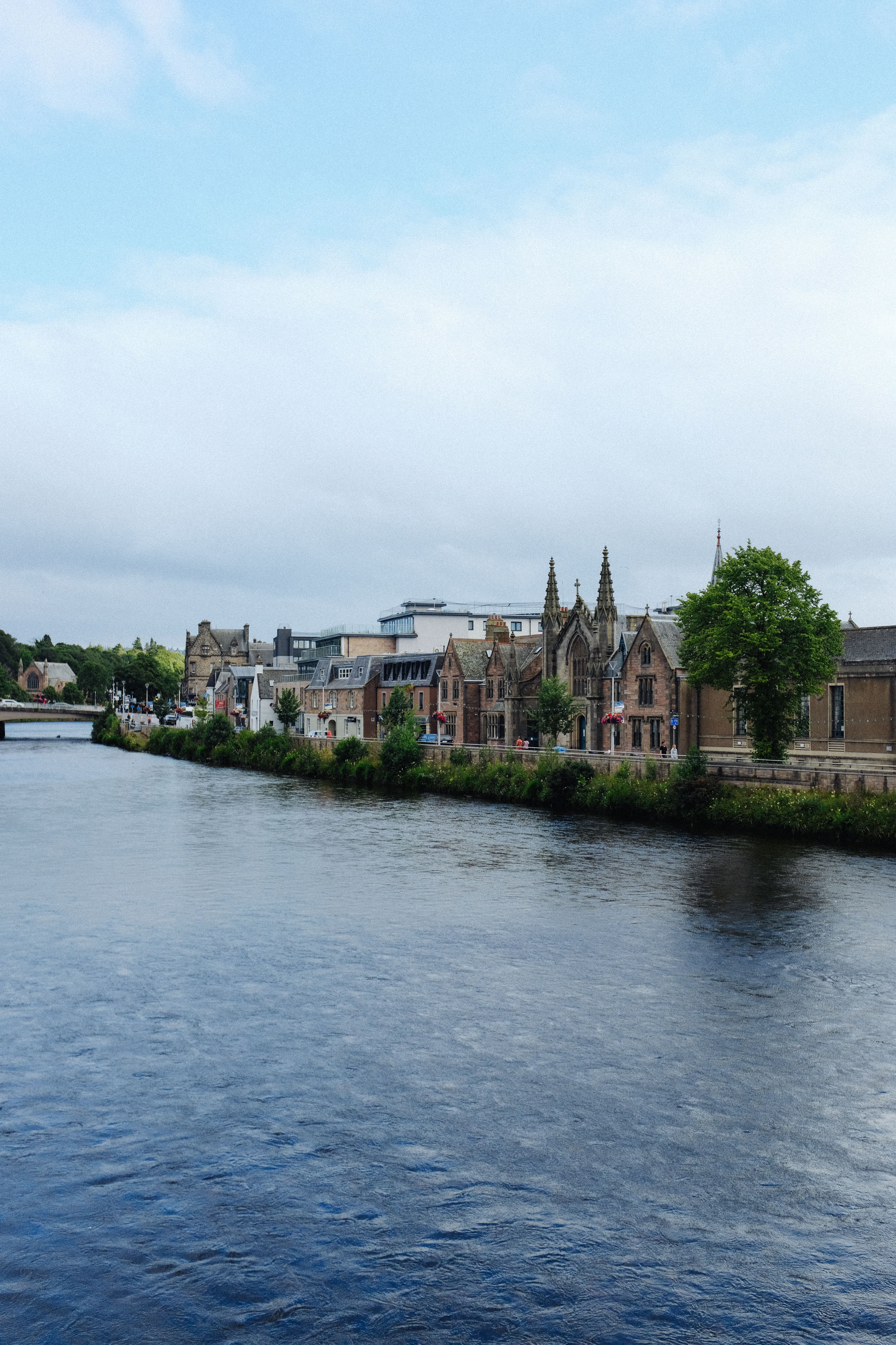 Picturesque view of historic buildings along River Ness in Scotland, capturing serene beauty.