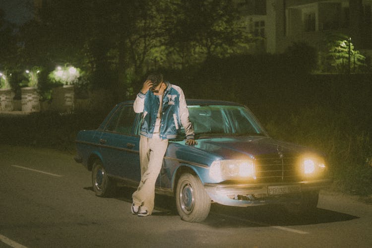 A Man Wearing Jacket Leaning On The Car