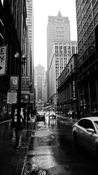 Black and white photo of a rainy city street with towering buildings in view.