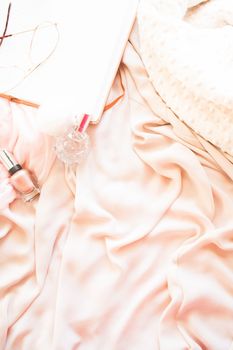 Delicate arrangement of pink fabric with eyeglasses, perfume, and book.