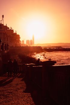 Silhouetted figures walk along Algiers' coastline during a vibrant sunset.