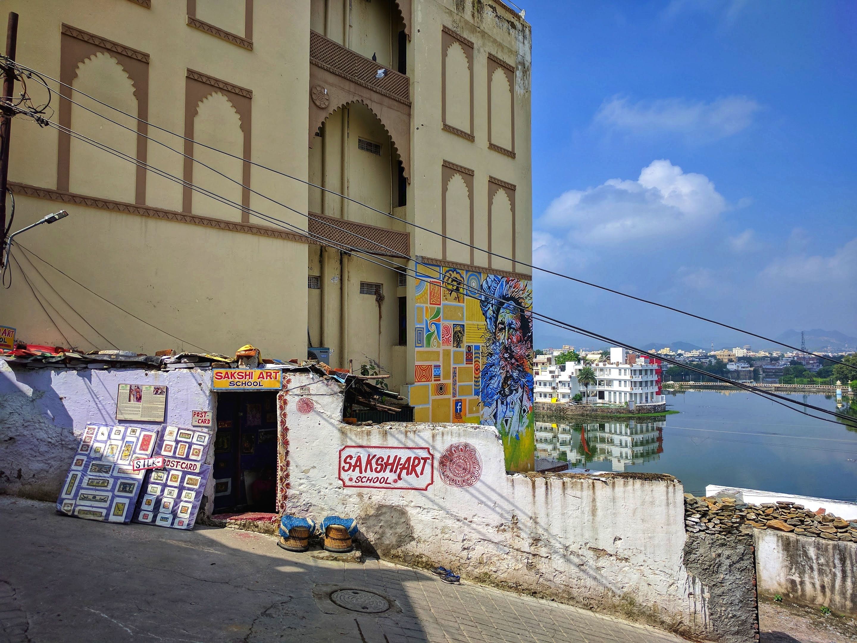 Vibrant Sakshi Art School entrance with mural by Udaipur lake on a sunny day.