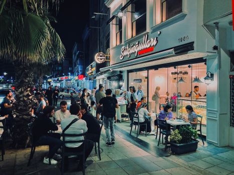 Nighttime scene at a bustling sidewalk cafe in Istanbul, Turkey, featuring diverse people enjoying the urban nightlife.