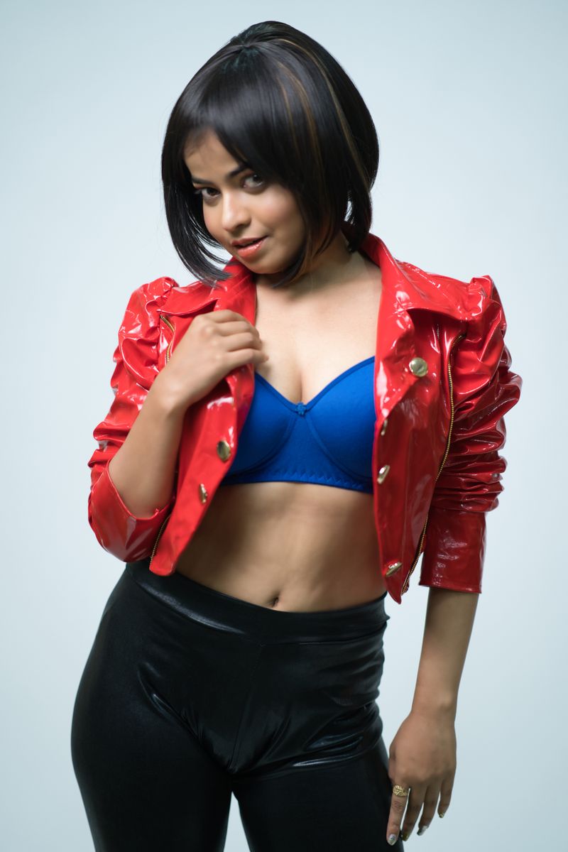 Confident woman posing stylishly in a red jacket and blue brassiere against a white background.