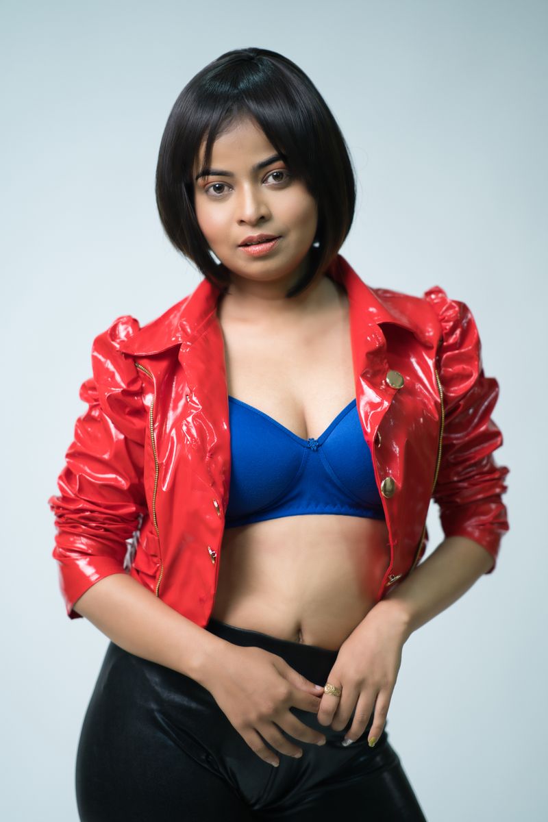 Stylish woman posing in a red leather jacket and blue top, studio portrait.