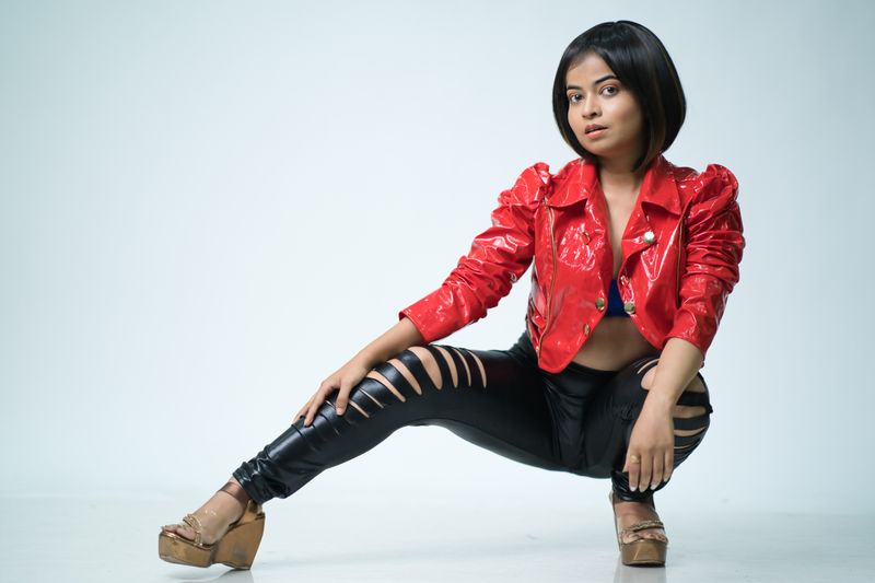 Trendy young woman in a red jacket and ripped pants posing on a white background.