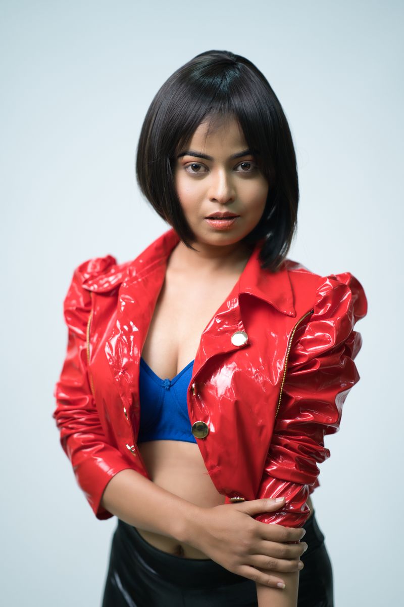 Woman in vibrant red leather jacket and blue top, studio setting.
