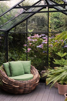 Relax in a wicker armchair amidst vibrant plants and flowers in a greenhouse sanctuary.