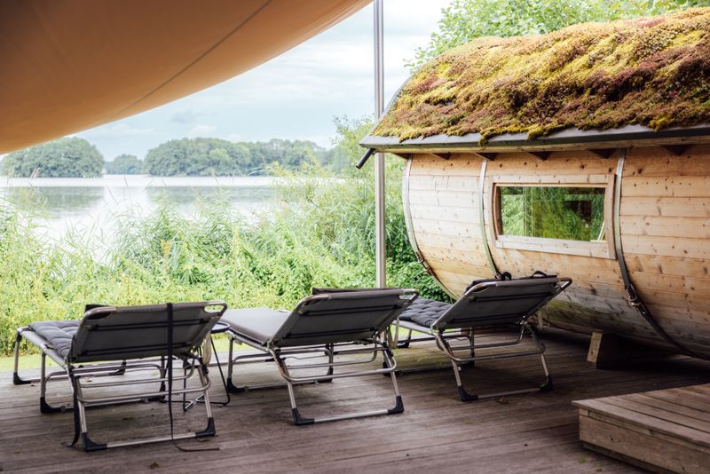 Relaxing lakeside sauna with moss-covered roof and sun loungers for outdoor Nordic wellness