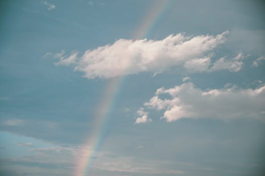 A serene sky showcasing a vibrant rainbow arcing through fluffy clouds.