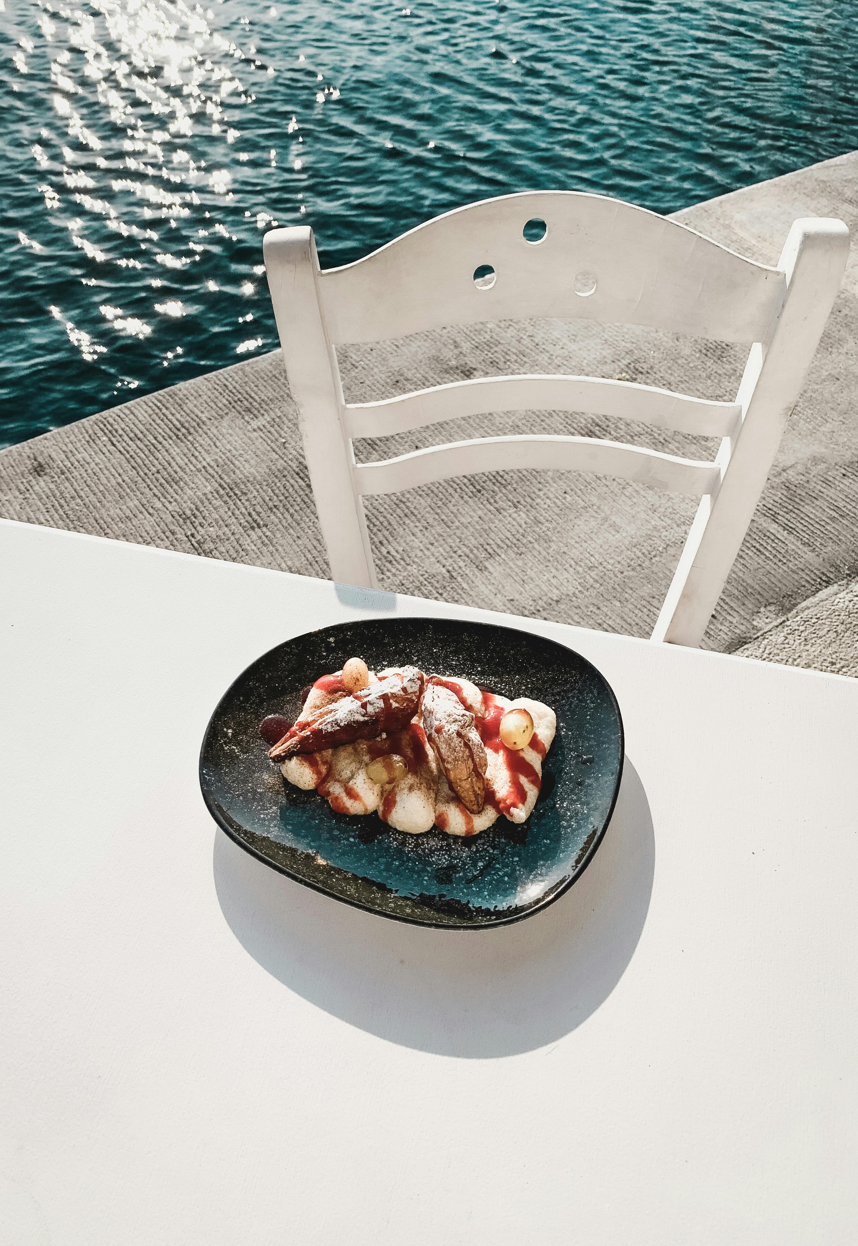 A beautifully styled plate of gelato with fruit toppings on a sunny day by a Greek waterside.