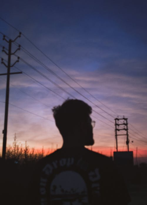 Silhouette of a Man Standing Near Power Lines