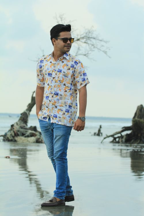 Free Stylish man in printed shirt and denim jeans standing by picturesque beach with driftwood. Stock Photo