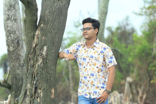 Free Man in floral shirt leaning on tree, enjoying a peaceful outdoor moment. Stock Photo