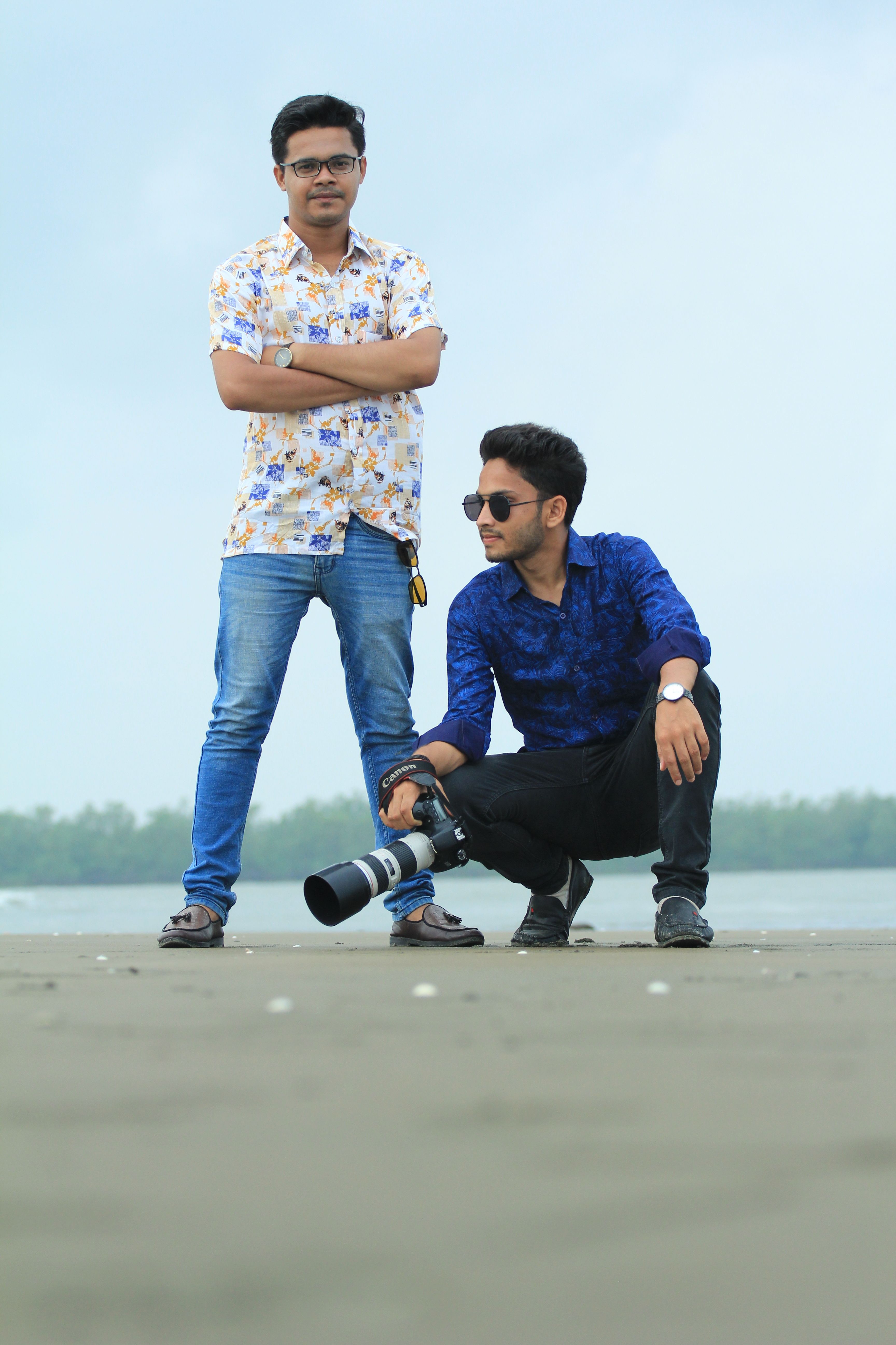 Two men on the beach, one with a camera, capturing moments against a serene shore.