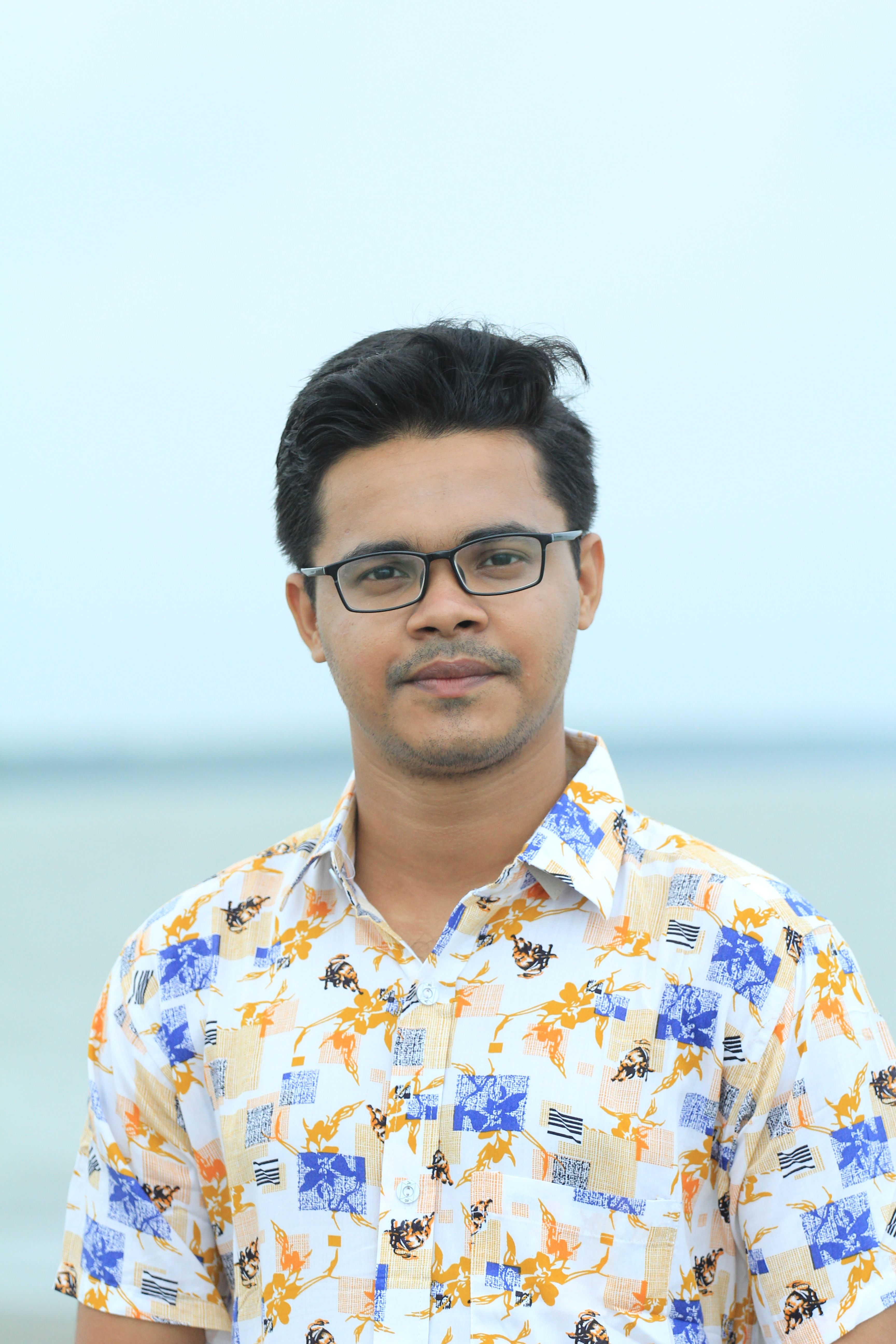 Close-up portrait of a stylish man in glasses with a printed shirt, standing outdoors.