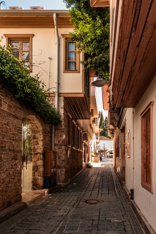 Free Explore a quaint alleyway lined with rustic buildings and vibrant greenery under soft daylight. Stock Photo