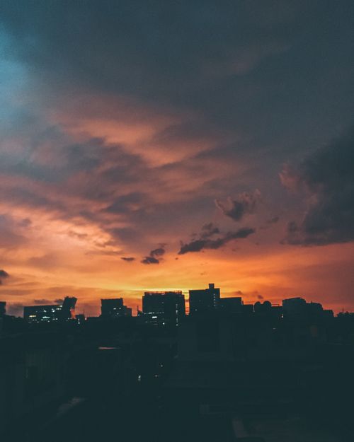 Free Silhouetted cityscape at sunset with dramatic clouds and vibrant hues. Stock Photo