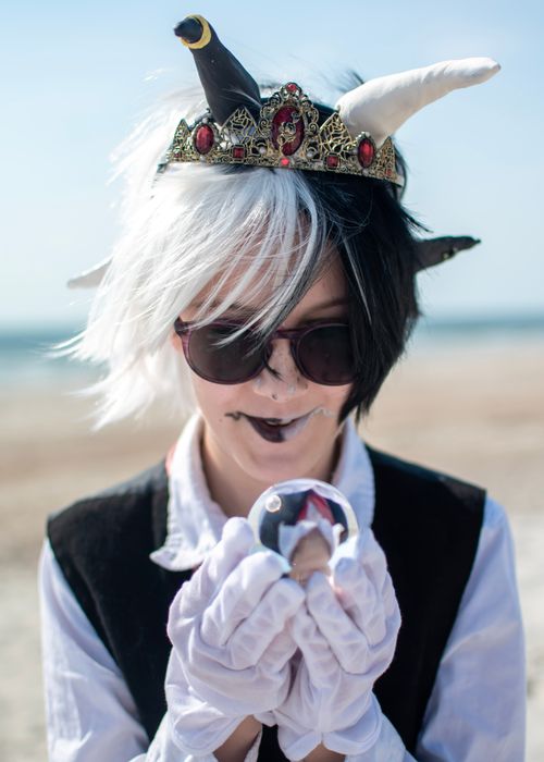 Free A creative fantasy cosplay portrait featuring a unique jester costume with sunglasses, set on a sunny beach. Stock Photo