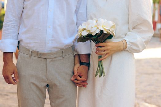 A couple in stylish attire holding hands with a bouquet, expressing love and togetherness.