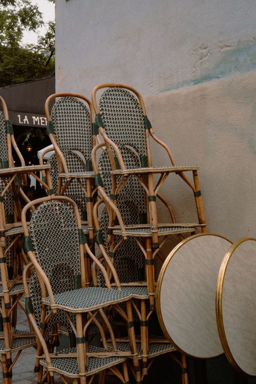 Free Stacked woven bistro chairs on a quaint Paris street, hinting at charm and local lifestyle. Stock Photo