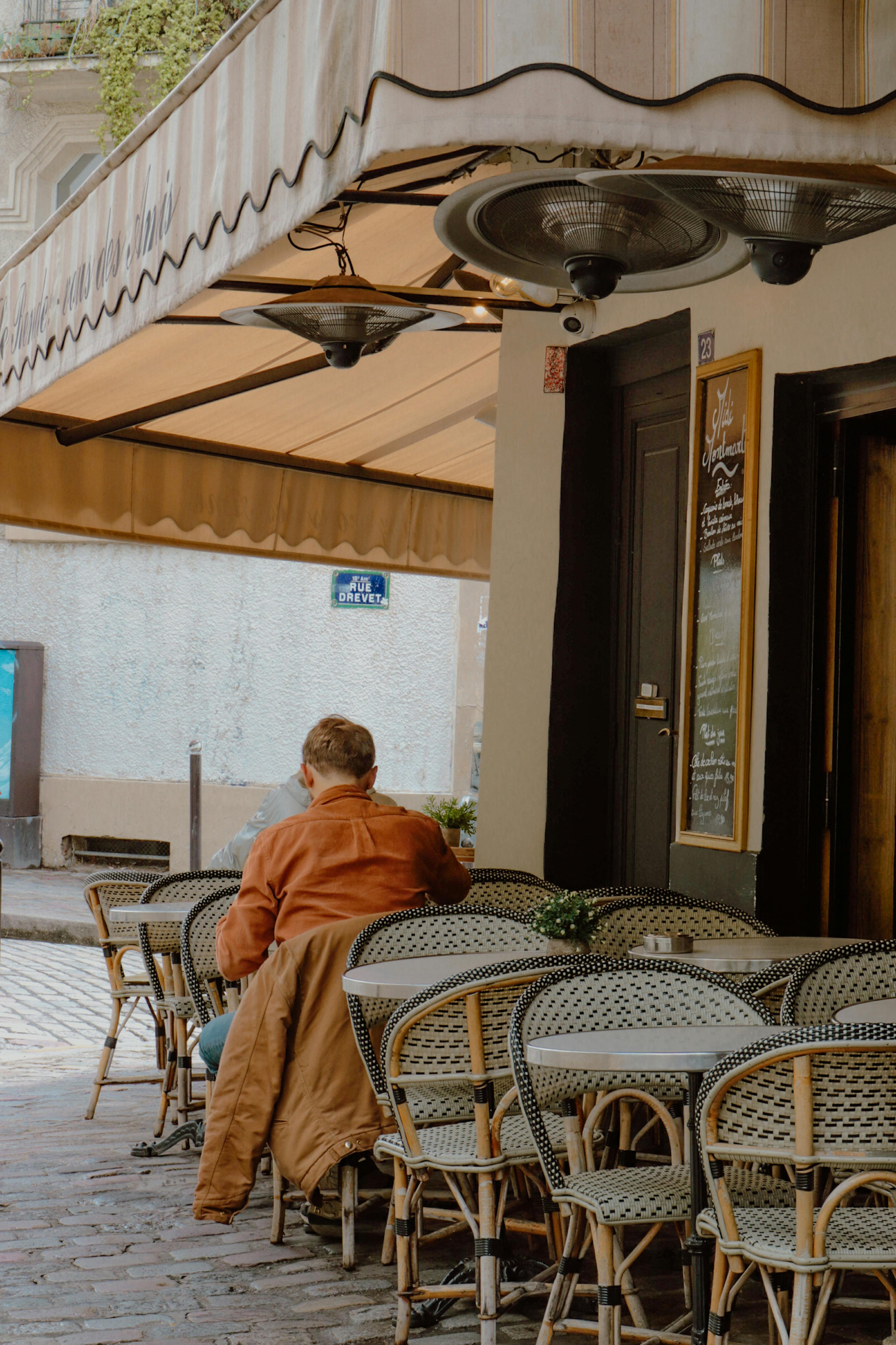 Back view of a man sitting alone at a charming outdoor Paris café, capturing the essence of Parisian life.