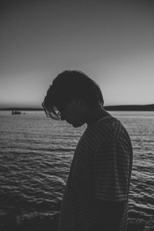 Free Silhouette of a man in a striped shirt by the sea at twilight, conveying a moody ambiance. Stock Photo