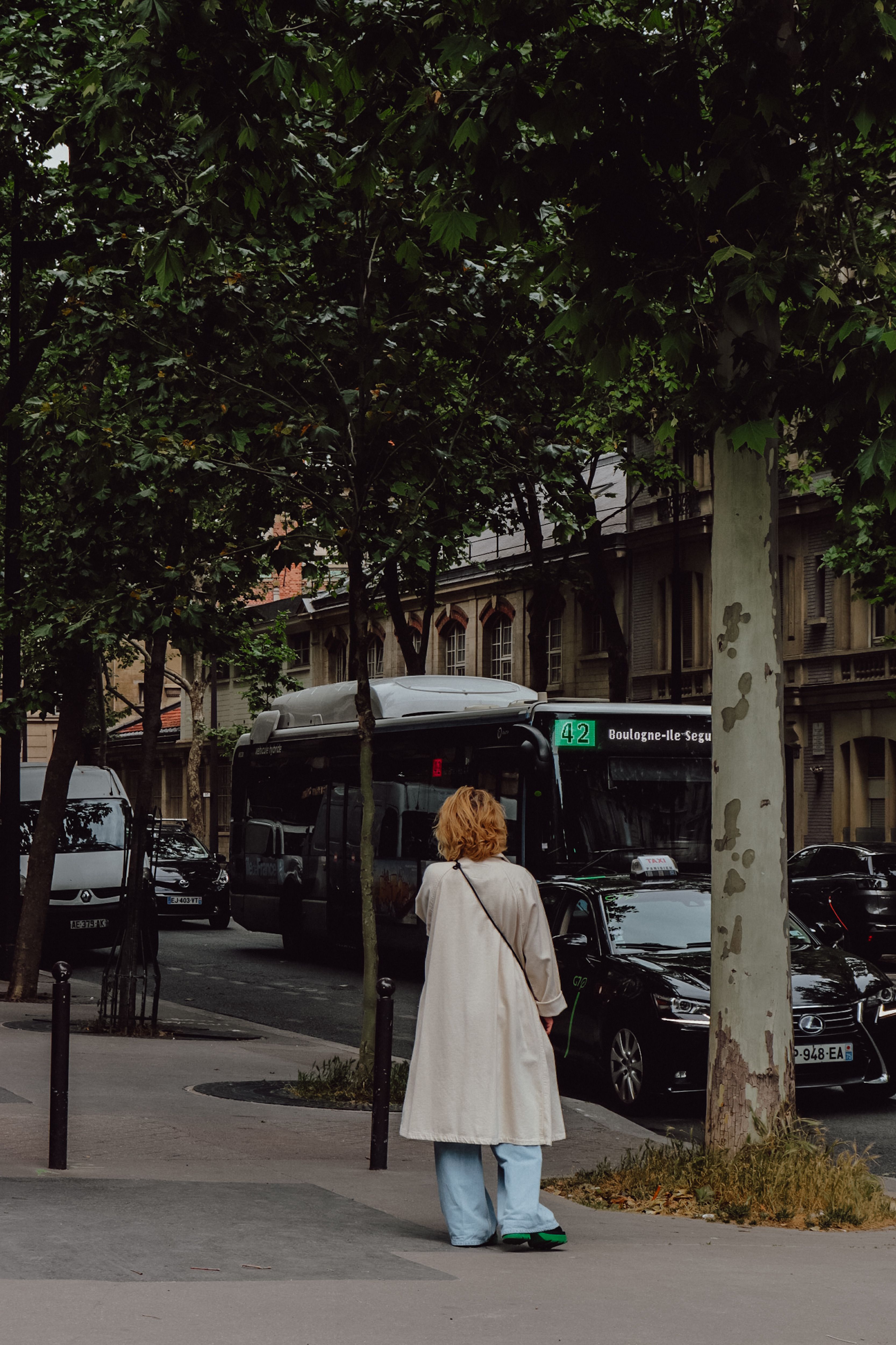 Back view of a person in a trench coat walking in Paris city street with vehicles.