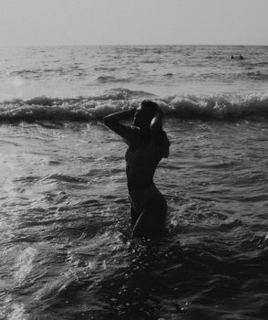 A woman silhouetted against ocean waves, enjoying a beach swim in a serene, black-and-white setting.