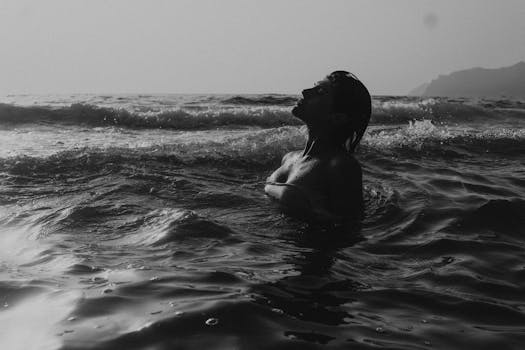 A dramatic black-and-white silhouette of a woman in ocean waves at twilight.